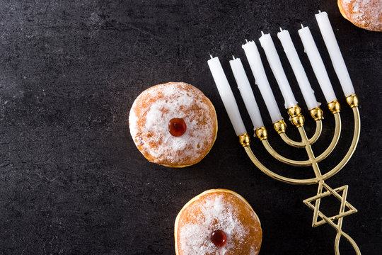 Jewish Hanukkah menorah and sufganiyot donuts on black background. Top view. Copy space