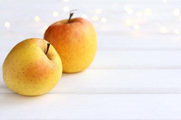two yellow-orange apples on the table against the background of festive lights. ripe autumn fruits