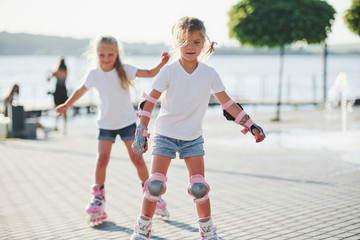 Two cute kids riding by roller skates in the park at daytime