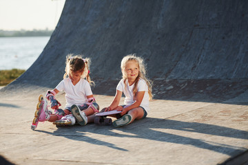 Relaxing and have conversation. On the ramp for extreme sports. Two little girls with roller skates outdoors have fun