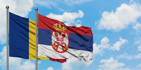 Romania and Serbia flag waving in the wind against white cloudy blue sky together. Diplomacy...