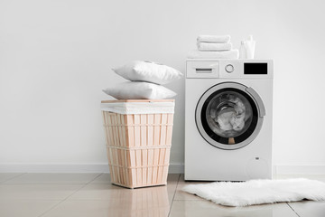 Modern washing machine with laundry near light wall