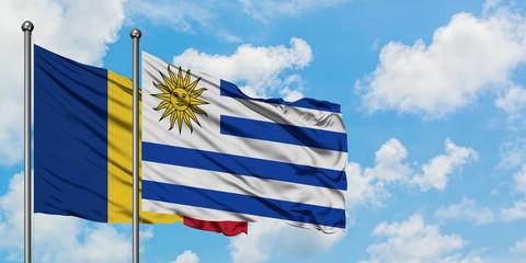 Romania and Uruguay flag waving in the wind against white cloudy blue sky together. Diplomacy...