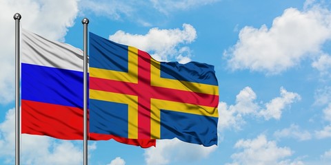 Russia and Aland Islands flag waving in the wind against white cloudy blue sky together. Diplomacy concept, international relations.