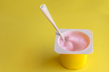 Strawberrry yogurt in yellow plastic cup with spoon isolated on bright yellow background with space for text