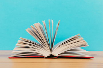 A simple composition of many hardback books, raw books on a wooden table and a bright blue background