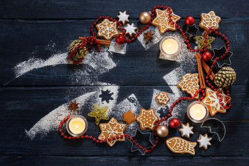 Obraz na płótnie Canvas Gingerbread cookies, Christmas baubles, decoration and burning candles on a falling star shape from icing sugar on a dark blue rustic wood, flat lay with copy space, high angle view from above