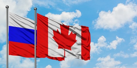 Russia and Canada flag waving in the wind against white cloudy blue sky together. Diplomacy concept, international relations.