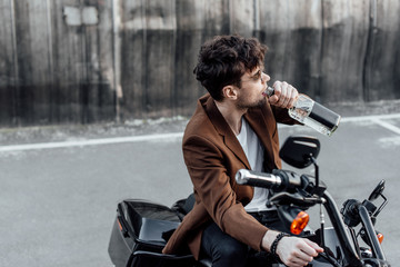 Fototapeta na wymiar man in brown jacket drinking alcohol from bottle while sitting on motorcycle