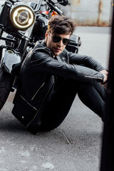handsome young man sitting on asphalt near motorcycle