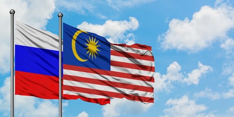 Russia and Malaysia flag waving in the wind against white cloudy blue sky together. Diplomacy concept, international relations.