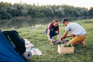 happy couple on camping by the river outdoor. setting up camping fire