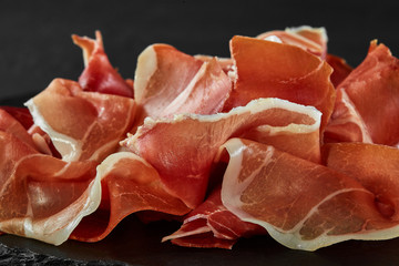 Gourmet, manually sliced jamon on black stone slate board against a dark grey background. Close-up...