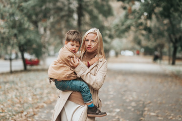 Fototapeta na wymiar mother and baby son playing and laughing on autumn walk. mom and son embracing outdoors on cloudy autumn day. Relationship between parent and son concept. Family emotions lifestyle