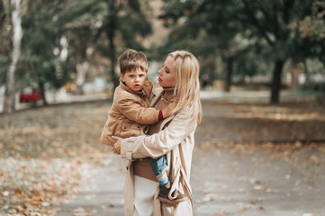 mother and baby son playing and laughing on autumn walk. mom and son embracing outdoors on cloudy...