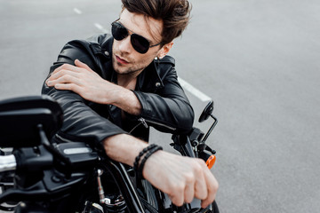 selective focus of cool man in sunglasses sitting on motorcycle and looking away