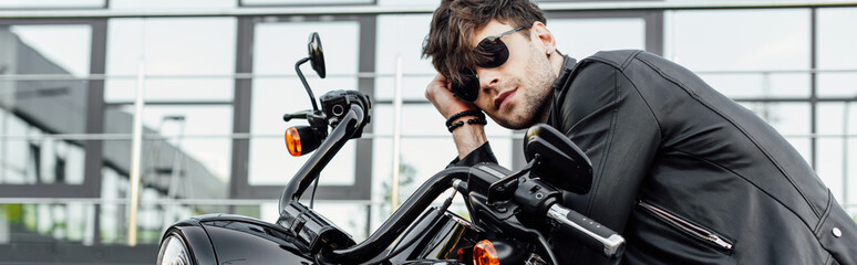 panoramic shot of handsome young man in leather jacket resting while sitting on motorcycle