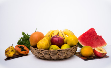 Several tropical fruits in a basket and spread all over a white table