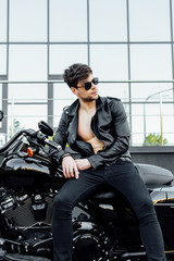 Obraz na płótnie Canvas front view of young man leaning on black motorcycle and looking away