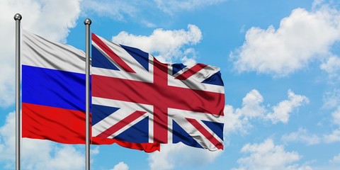 Russia and United Kingdom flag waving in the wind against white cloudy blue sky together. Diplomacy concept, international relations.