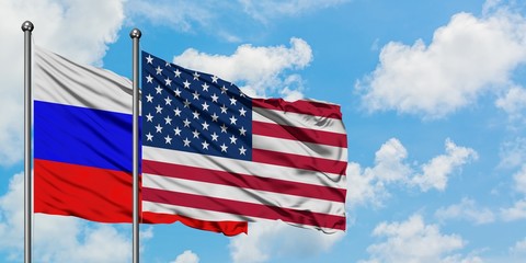 Russia and United States flag waving in the wind against white cloudy blue sky together. Diplomacy concept, international relations.