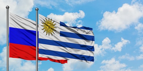 Russia and Uruguay flag waving in the wind against white cloudy blue sky together. Diplomacy concept, international relations.