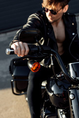 selective focus of young man sitting on motorcycle in sunlight, holding handle and looking away
