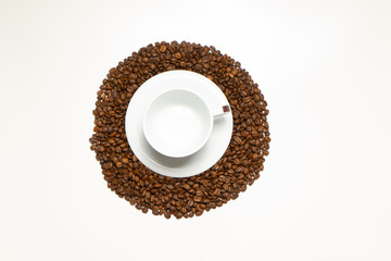 White cup with coffee and plate in the pile of coffee beans on the white wooden background. Food and drink background photography.