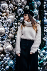  young woman in warm oversize sweater posing near christmas decorations outdoor