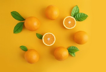 Oranges fruits composition with green leaves and slice on yellow background, copy space.