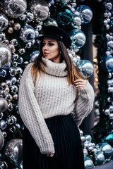  young woman in warm oversize sweater posing near christmas decorations outdoor