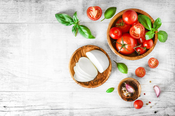 Fresh finest tomatoes on white rustic board with basil and mozzarella cheese top view.