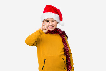 Little boy celebrating christmas day wearing a santa hat isolated showing a horns gesture as a revolution concept.