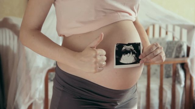 Close-up shot of big pregnant tummy and woman's hands holding ultrasound image of healthy unborn baby. Women's health and people concept. Maternity prenatal care and woman pregnancy concept. 