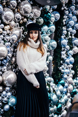 young woman in warm oversize sweater posing near christmas decorations outdoor
