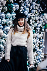  young woman in warm oversize sweater posing near christmas decorations outdoor
