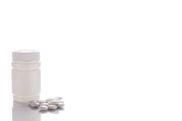 A jar of poured tablets stands on a mirror surface on a white background on the left side.