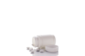 A jar with poured tablets and an open lid lies on a mirror surface on a white background in the middle.
