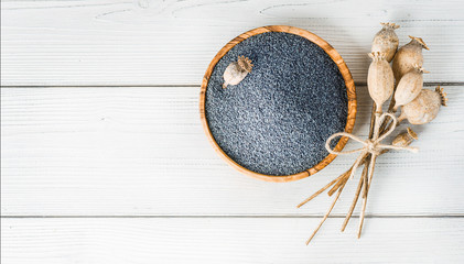 Poppy seeds in wooden bowl from top view. Poppies head on white table.