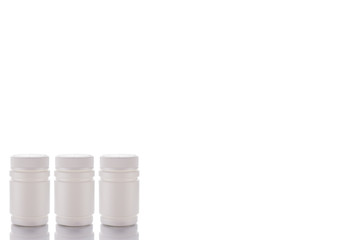 Three jars of pills and closed caps stand on a mirror surface on a white background on the left side.