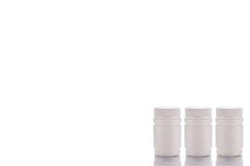 Three jars of pills and closed caps stand on a mirror surface on a white background on the right side.