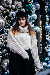  young woman in warm oversize sweater posing near christmas decorations outdoor