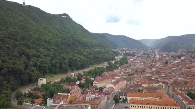 Aerial view of Brasov city, medieval town situated in Transylvania, Romania. Old architecture surrounded with big Carpathian mountains covered with dense green forest.
