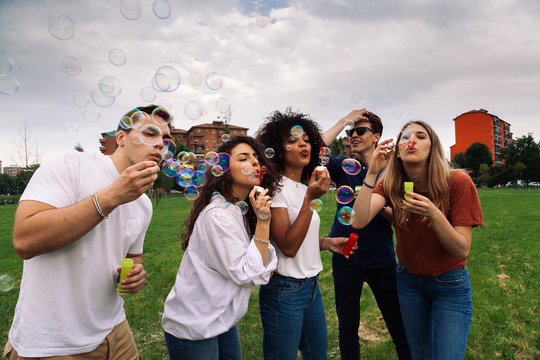 Group of young friends in a park at sunset - Millennials have fun on a summer afternoon with soap bubbles
