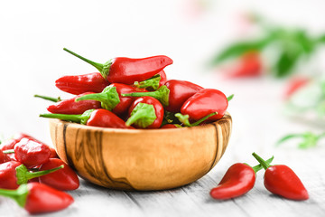 Red hot chili peppers in wooden bowl side view. Hot spicy pepper detail on white rustic table.