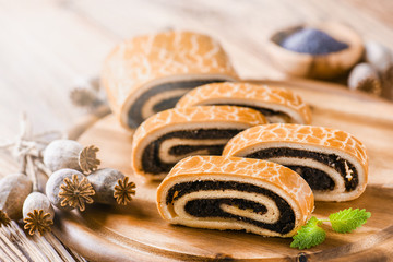 Poppy roll cake on wooden rustic table. Traditional christmas strudel with poppies heads and seed in background.