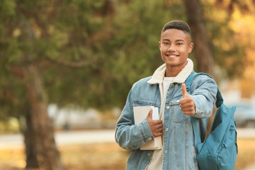 Fototapeta premium Portrait of teenage African-American student showing thumb-up outdoors
