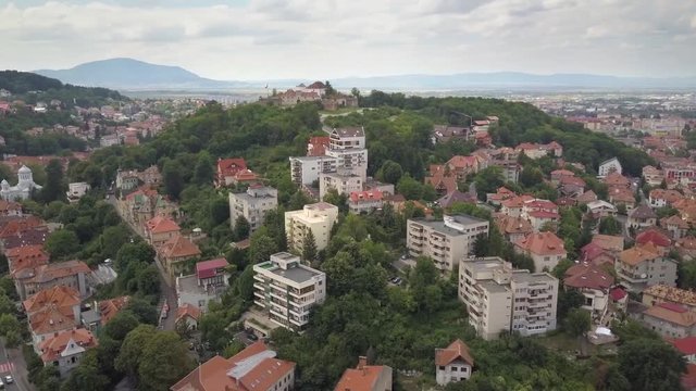 Aerial view of Brasov city, medieval town situated in Transylvania, Romania. Old architecture surrounded with big Carpathian mountains covered with dense green forest.