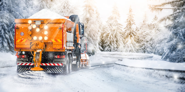 Snow plow on highway salting road . Orange truck deicing street. Maintenance winter vehicle wide panorama or banner.