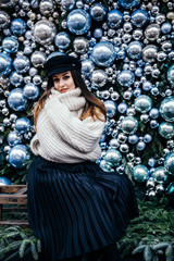  young woman in warm oversize sweater posing near christmas decorations outdoor